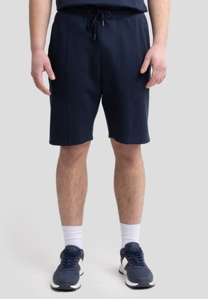 Navy shorts made of soft fabric, featuring a drawstring waistband, front pockets, and a knee-length cut, paired with athletic shoes.