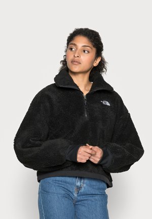 Pull en polaire noir avec un col montant, fermeture éclair demi-ventrale et poignets côtelés. Caractérisé par un logo sur la poitrine. Tissu doux et texturé.