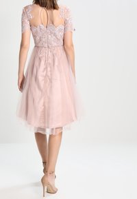 Krátké růžové šaty s krajkovým korzetem a krátkými rukávy, tylová sukně sahající pod kolena a detail klíčové díry na zádech.