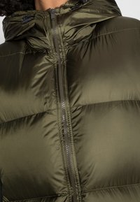 Giubbotto imbottito verde oliva con una finitura lucida, dotato di chiusura con zip e cappuccio regolabile con cordino. Design trapuntato testurizzato visibile.