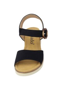 Czarne zamszowe sandały z szerokim paskiem z przodu, regulowanym paskiem na kostkę i dekoracyjną brązową klamrą. Kremowa podeszwa z przeszyciem.