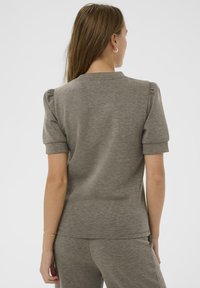 Siva majica s kratkim rukavima i okruglim izrezom, teksturirana tkanina i napuhani rameni dijelovi. Stražnji prikaz pokazuje glatke šavove i opušteni kroj.