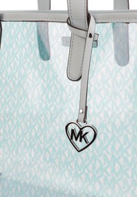 Genomskinlig tote-väska i ljusblått med ett upprepat mönster av vita MK-logotyper. Har grå läderhandtag och en hjärtformad logocharm.