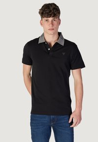 Polo negro con un cuello y logo grises contrastantes, que presenta una tapeta de tres botones y mangas cortas. La tela parece suave y ajustada.