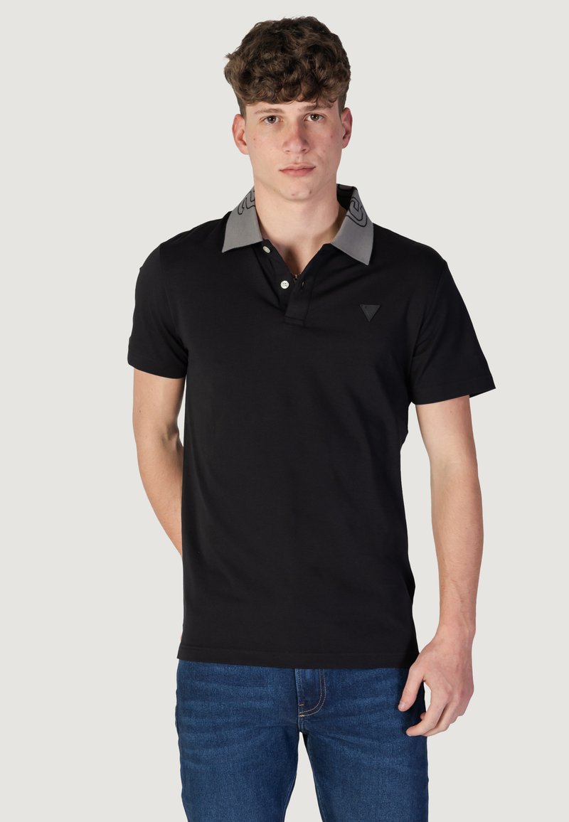 Polo negro con un cuello y logo grises contrastantes, que presenta una tapeta de tres botones y mangas cortas. La tela parece suave y ajustada.