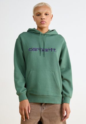 Sudadera verde oscuro con un bolsillo frontal y el logo "carhartt" en púrpura. Cuenta con capucha ajustable y puños y dobladillo de canalé. Textura suave.