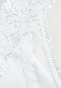 White lingerie featuring intricate floral lace trim along the edges, soft satin fabric, and a smooth texture. Accents of delicate patterns.