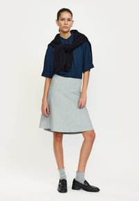 Completo femminile con camicetta blu scuro, gonna svasata grigio chiaro, maglione nero annodato sulle spalle, calzini grigi e mocassini neri.