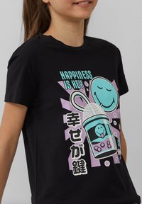 Kind dat een zwart T-shirt draagt met een kleurrijke afbeelding van een lachende bubble tea-kop en tekst "Happiness is key" in het Engels en Japans.