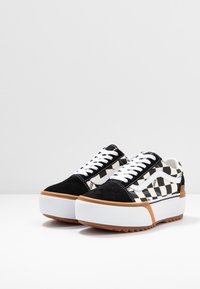 Zapatillas de cuadros en blanco y negro con parte superior de ante y lona, cordones blancos, suela gruesa de plataforma blanca y suela de goma natural.