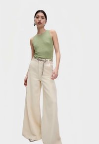 Zielony top bez rękawów o fakturowanym wykończeniu, zestawiony z wysokim stanem, szerokimi kremowymi spodniami, akcentowany srebrnym paskiem z łańcuszkiem.