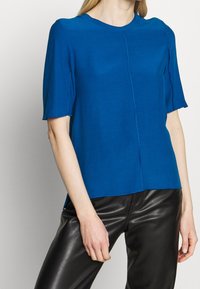 Niebieski top z krótkim rękawem i okrągłym dekoltem, o prostym kroju z subtelnymi detalami szwów. Połączony z czarnymi skórzanymi spodniami.
