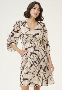 Robe avec un décolleté en V, des manches trois-quarts et un motif abstrait noir et beige. Comprend des plis doux et des poches sur les côtés.