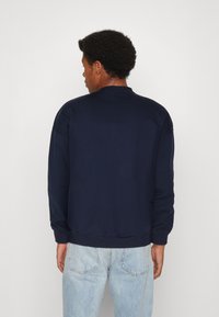 Sudadera de color azul marino con cuello redondo y puños acanalados. El diseño presenta un corte relajado, tejido texturizado y un estilo minimalista.