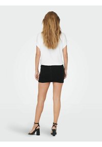 Minifalda de denim negro, diseño ajustado, cintura alta, combinada con una blusa de manga corta blanca. Tacones negros con tiras complementan el look.