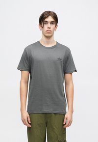T-shirt de algodão cinza com decote redondo, mangas curtas e um pequeno logótipo no peito. Combinado com calças cargo verde-oliva.
