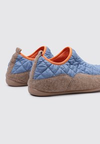 Parte superior acolchada en azul con acentos en naranja y sección inferior de fieltro gris. Forma redondeada con una lengüeta trasera y suela de goma marrón.