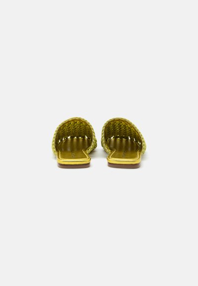Paire de sandales plates dorées à talon ouvert, avec des brides entrelacées et un détail carré à l'avant, présentée sur fond blanc.