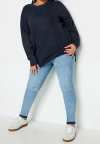 Dunkelblaues geripptes Sweatshirt mit langen Ärmeln, kombiniert mit hellblauen engen Jeans und weißen Turnschuhen mit braunen Sohlen.