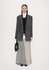 Blazer grigio doppiopetto sopra una maglietta nera, camicia bianca e una lunga gonna di jeans patchwork. Una borsa nera e scarpe completano il look.