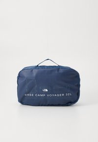 Sötétkék párnázott táska felső fogantyúval, h�árom tárolási lehetőséget bemutató grafikai tervezéssel. A szöveg olvasható: "BASE CAMP VOYAGER 32L."