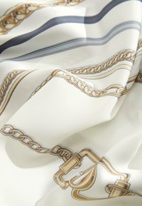 Weißer Seidenstoff mit einem Muster aus goldenen und marineblauen Ketten und Schnallen, mit glatter Textur und glänzendem Finish.