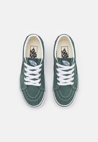 Ett par gröna Vans-sneakers med vita snören, svarta sidostreifen och "Vans Off The Wall"-logotyp på tungan och innersulorna.