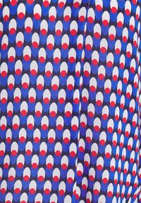 Motif répétitif de formes ovales en blanc, bleu et rouge sur un tissu foncé avec un léger pli visible près du centre.