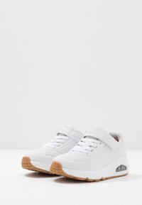 Witte sportschoenen met een geperforeerd ontwerp, een gevoerde zool, een verstelbare riem en een gumrubberen loopzool. Bevat een zichtbare luchtunit.