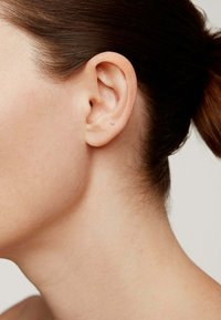 Pequeño pendiente de stud en una oreja perforada. El pendiente está colocado cerca del lóbulo, con un diseño metálico simple y un acabado brillante.