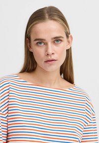 T-shirt rayé avec des lignes horizontales rouges, bleues et blanches, dotée d'un large décolleté et de manches courtes, fabriquée en coton doux.