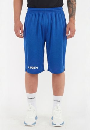 Uomo che indossa pantaloncini sportivi blu, calzini bianchi, scarpe da ginnastica bianche e una maglietta nera, in piedi su uno sfondo bianco uniforme.