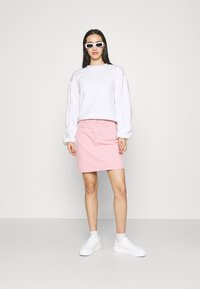 Pullover branco com mangas bufantes, saia de ganga rosa e ténis brancos. Os acessórios incluem óculos de sol retangulares brancos.