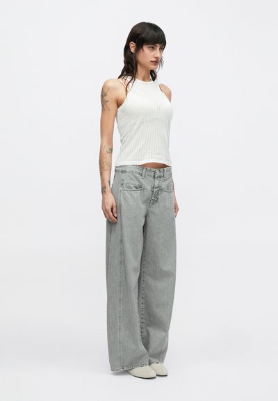 Λευκό ριμπ τοπ με αμάνικη σχεδίαση, σε συνδυασμό με άνετο, ανοιχτό γκρι τζιν παντελόνι και μπεζ παπούτσια τύπου slip-on. Η εμφάνιση χαρακτηρίζεται από μίνιμαλ σχεδιασμό και casual εφαρμογή.