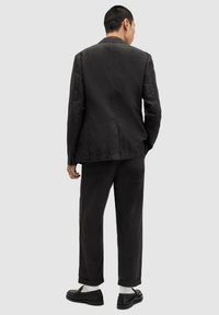 Black structured jacket with a straight cut, paired with matching trousers. Material appears lightweight, creating a relaxed, minimalist look.