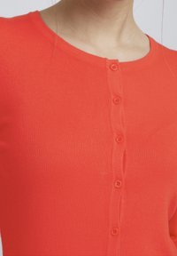 Cárdigan de punto acanalado rojo con cuello redondo, seis botones a juego en la parte delantera y un diseño ajustado.