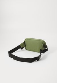 Πράσινη καμβά τσάντα μέσης με ορθογώνιο σχήμα, δύο θήκες με φερμουάρ και ρυθμιζόμενο μαύρο λουρί. Υφασμάτινη υφή.