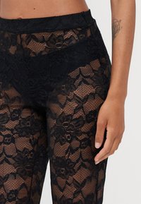 Leggings neri in pizzo caratterizzati da motivi floreali, una finitura testurizzata e una vita elasticizzata. Vista ravvicinata che mette in evidenza il design intricato.