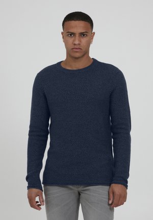 Marineblauer strukturierter Strickpullover mit langen Ärmeln, Rundhalsausschnitt und taillierter Silhouette. Tragen mit hellgrauen Jeans.
