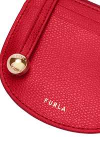 Red leather cardholder with a textured surface, gold logo, and hardware accents. Features slots for cards and a rounded shape.