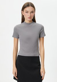 Grå tætsiddende T-shirt med korte ærmer og høj hals. Ribbet tekstur, parret med en sort nederdel. Enkel design uden udsmykninger.