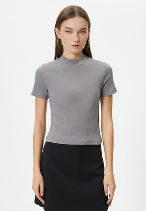 Grå tætsiddende T-shirt med korte ærmer og høj hals. Ribbet tekstur, parret med en sort nederdel. Enkel design uden udsmykninger.