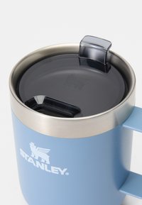 Niebieski kubek ze stali nierdzewnej z srebrną krawędzią, ma czarną plastikową pokrywkę i otwór do picia. Logo widoczne z przodu.