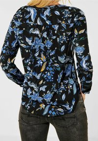 Blusa nera con motivi floreali blu e gialli, maniche lunghe e design con pieghe sul retro. Realizzata in tessuto leggero, dalla morbida texture.