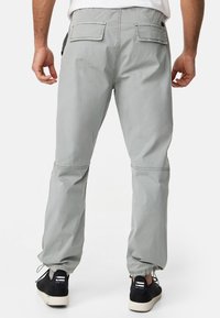 Pantalon cargo gris avec poignets ajustables, poches latérales et poches arrière. Fabriqué en tissu léger avec une texture lisse.
