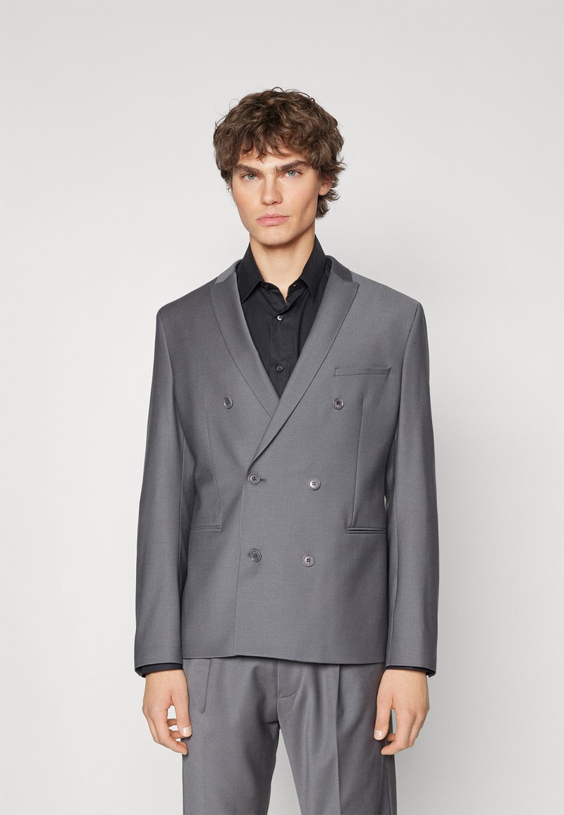 Grå dobbelspent blazer med notch-lapel, med subtile svarte detaljer. Laget av glatt stoff, den har to frontlommer.