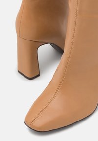 Bottines à talons hauts en cuir tan avec un bout pointu, des coutures marquées et un talon bloc. Texture lisse avec un design épuré.
