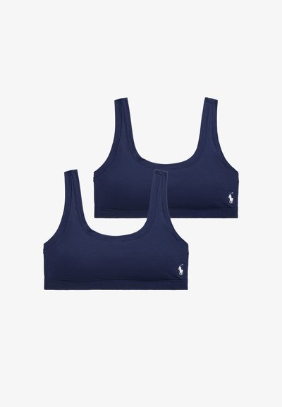 Dvě sportovní podprsenky v námořnicky modré barvě s bezešvým designem, širokými ramenními popruhy a malým bílým logem na levé straně. Materiál z bavlněné směsi.