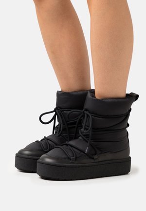 Black padded boots with a rounded toe, adjustable laces, and a thick black outsole, featuring a soft texture and a mid-height design.