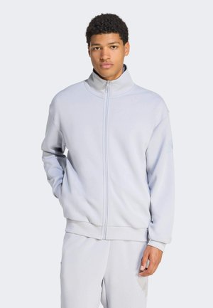 Jasnoszara kurtka na zamek wykonana z miękkiej tkaniny, z wysokim kołnierzem i ściągaczami na rękawach. Projekt zawiera subtelne logo na rękawie.